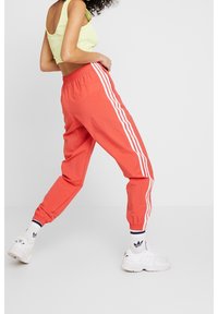 Korallfärgade joggers med vita sidostripes, resårmidja och avsmalnande muddar, kombinerade med en limegrön crop top och vita sneakers.