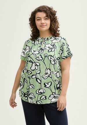 Bloemmotief korte mouwen top in groen met zwarte en witte bloemen, voorzien van een keyhole halslijn. Soepele textuur, losse pasvorm.
