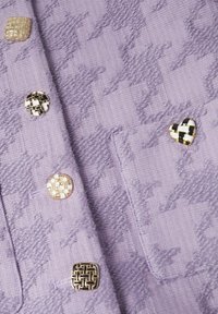 Tissu texturé lilas avec grand motif pied-de-poule, comportant cinq boutons décoratifs de formes variées et designs en noir, blanc et or.