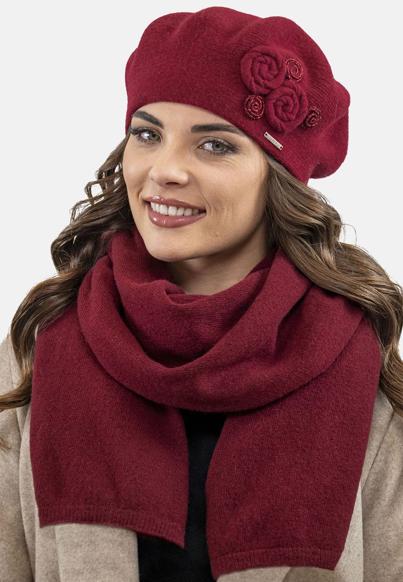 Berretto lavorato a maglia color borgogna con tre rose di tessuto e sciarpa dello stesso colore, caratterizzati da una morbida texture e uno stile drappeggiato.