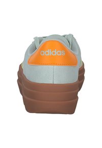 Adidas sneaker met een mintgroene bovenkant, oranje hielstrap, bruine rubberen zool en reflecterende gele accenten. Zachte textuur en ronde vorm.