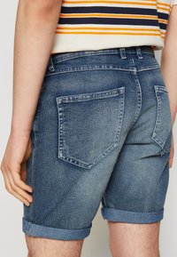 Shorts de mezclilla en azul claro, con dobladillo enrollado, dos bolsillos traseros y un corte clásico con un leve desgaste en la tela texturizada.