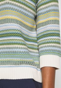 Gebreide trui met meerkleurige strepen in groen, blauw, geel en crème; ribgebreide mouwen en onderrand in crème; gestructureerd patroon overal.