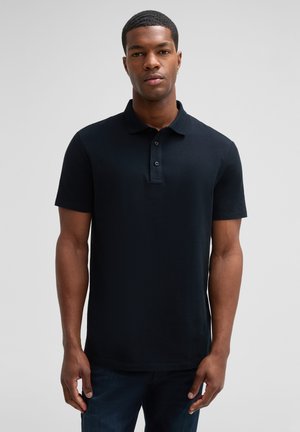 Schwarzes Polohemd aus strukturiertem Stoff, kurze Ärmel, mit einer Drei-Knopf-Leiste und einem normalen Kragen. Getragen mit dunkelblauen Jeans.