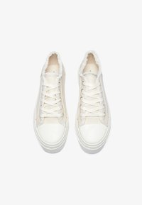 Baskets blanches avec une surface lisse et brillante, des accents en tissu texturé et un col en fourrure douce. Comprend un laçage standard et une semelle en caoutchouc.