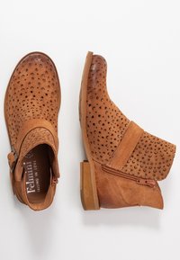 Bottes basses en daim marron avec texture perforée, fermeture éclair latérale et petit talon en bois. Dotées d'une boucle décorative sur la sangle.