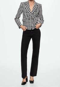 Černobílý houndstooth dvouřadý blazer s špičatými klopami; v kombinaci s černými rovnými džínami a černými lodičkami s špičatou špičkou.
