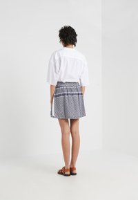 Camisa blanca de manga corta, falda azul marino con estampado geométrico y sandalias marrones. La falda tiene pliegues y acentos de ribete en contraste.