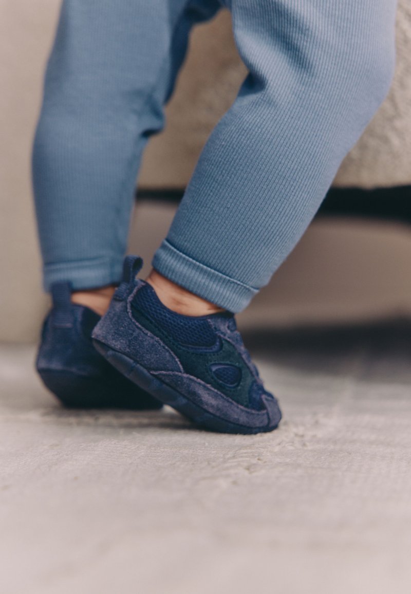 Chaussures pour enfants bleu marine combinant mesh et daim, avec une semelle en caoutchouc flexible et une languette à l'arrière.