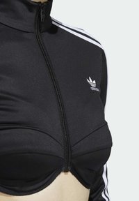 Black athletic crop jacket with high collar, zip fastening, and white accent stripes. Features a structured design with a fitted silhouette.