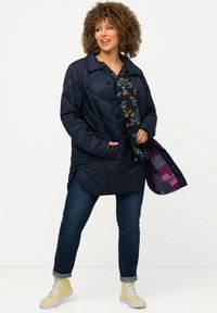 Námořnická prošívaná bunda s límcem, třemi knoflíky a bočními kapsami; vzorovaná vnitřní podšívka. Nosená přes květinový námořnický top a džíny.