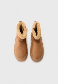 Bottes de cheville en suédine marron avec doublure en faux fourrure beige, bout rond, semelle en caoutchouc et coutures décoratives près du bord.