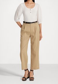White short-sleeve top with three buttons, paired with high-waisted beige pants and black strappy wedge sandals. Smooth fabrics and structured fit.