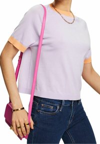Krótki rękaw, jasnofioletowa bluzka z pomara�ńczowym wykończeniem, zestawiona z ciemnoniebieskimi dżinsami. Różowa torba na ramię zwisa na ramieniu, dodając stylizacji akcentu.