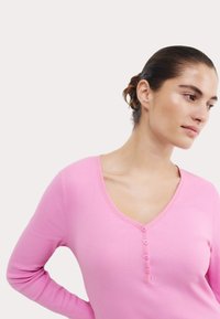 Rosa ribbade långärmade topp med V-ringning, prydd med fem knappar framtill och kontrasterande sömnad längs halsringningen.