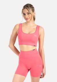 Roze sportset bestaande uit een naadloze, aansluitende crop top en shorts met hoge taille, beide gemaakt van zachte, rekbare stof met minimalistische logo-accenten.