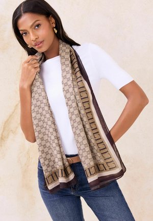 Könnyű, bézs színű sál kör alakú mintával és barna szegéllyel; puha textúrájú; fehér felső és kék farmer felett a nyak köré terítve.