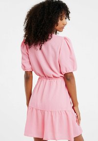 Abito rosa a maniche corte con maniche a palloncino, vita cinchata e orlo smerlato. Realizzato in un materiale strutturato, presenta un design semplice e fluido.