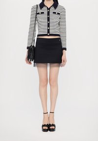 Striped, cropped navy and white sweater with buttons, paired with a black mini skirt featuring a sheer hem. Black platform sandals and fringe bag.