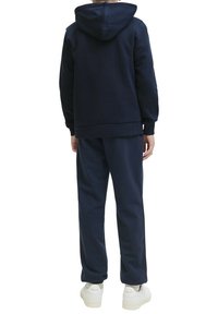 Sweatshirt à capuche bleu marine et pantalon de survêtement assorti. Tissu doux, coupe décontractée, poignets côtelés et poche kangourou. Baskets blanches.