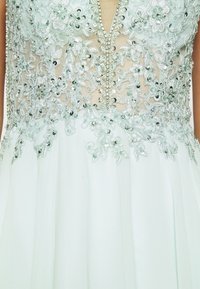 Světle modré šaty s propracovanou květinovou výšivkou, flitry a hlubokým výstřihem do V, dodatkové průsvitné vrstvy a splývavou sukni.