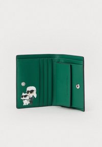 Zelená kožená peněženka otevřená, ukazující šest slotů na karty, patentku a nástěnné figurky osoby a psa v slunečních brýlích.