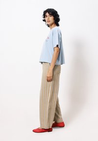 Hellblaues Baumwoll-Crop-Top mit kurzen Ärmeln, kombiniert mit beigen und weißen gestreiften weiten Hosen und roten Ballerinas.