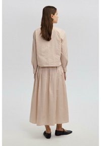 Krémovo-hnedý pruhovaný dvojdielny outfit s krátkym topom s dlhými rukávmi a plisovanou sukňou po členky. Čierne ploché topánky.
