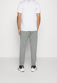 Grå sportiga joggers och en vit t-shirt med kort ärm och en svart logotyp på ryggen, tillsammans med svarta och vita sneakers.