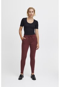Svart kortärmad topp och bordeauxfärgade högmidjade joggers med dragsko. Joggers har sidofickor och en åtsittande design. Svarta loafers.