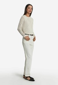 Vit långärmad topp i spetsstickning, högmidjade vita byxor och svarta flätade ballerinas med spänne.