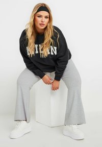 Svart sweatshirt med "MILAN" tryckt i vitt, gråsvarta svettbyxor med utsvängd design och vita platåskor. Håret stylat med ett svart pannband.