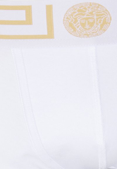 Witte katoenen slips met een gele logoband, versierd met een Grieks sleutelpuntpatroon en een gedetailleerd rond Medusa-embleem.