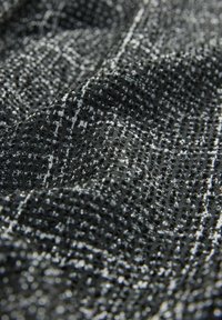 Tissu tissé en noir et blanc avec une surface texturée, présentant un motif à carreaux. Le matériau est composé de fils fins et d'une profondeur variable.