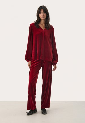 Velvet red loungewear set featuring a long-sleeve V-neck top and wide-leg pants, with gathered cuffs and a soft, smooth texture.