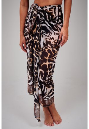 Vrouw die een sarong met luipaard- en zebraprint rond haar middel draagt, blootsvoets staand op een eentonige achtergrond.