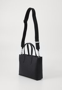 Black tote bag with a textured surface and logo pattern, featuring two handles and an adjustable strap, chrome hardware, rectangular shape.