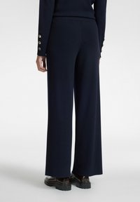 Meri siniset leveälahkeiset housut, jotka on valmistettu pehmeästä kankaasta, jossa on sileä pinta ja istuva vyötärö, yhdistettynä ruskeisiin paksupohjaisiin kenkiin.