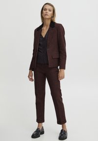 Blazer à carreaux bourgogne avec col noir, associé à une blouse à motifs noirs et un pantalon assorti ; des mocassins en cuir élégants complètent le look.