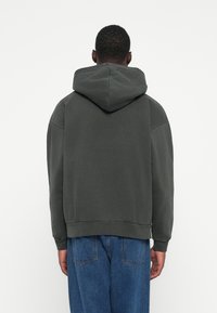 Mørkegrøn hoodie, blødt stof, afslappet pasform, har en stor hætte og ribbet kant. Sammen med lyseblå denim jeans.