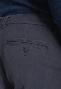 Dunkelgraue Hose aus strukturiertem Stoff mit einer flachen Gesäßtasche und einem schwarzen Knopfverschluss. Der Bund verfügt über eine Schlaufe zur Verstellbarkeit.