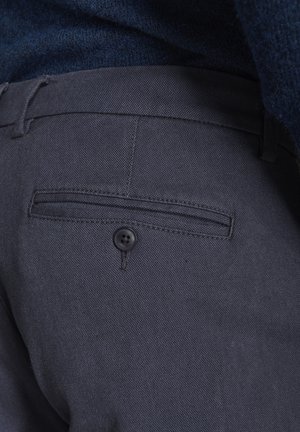 Pantaloni grigio scuro con tessuto strutturato, tasca posteriore piatta e chiusura con bottone nero. La vita include un passante per la regolazione.
