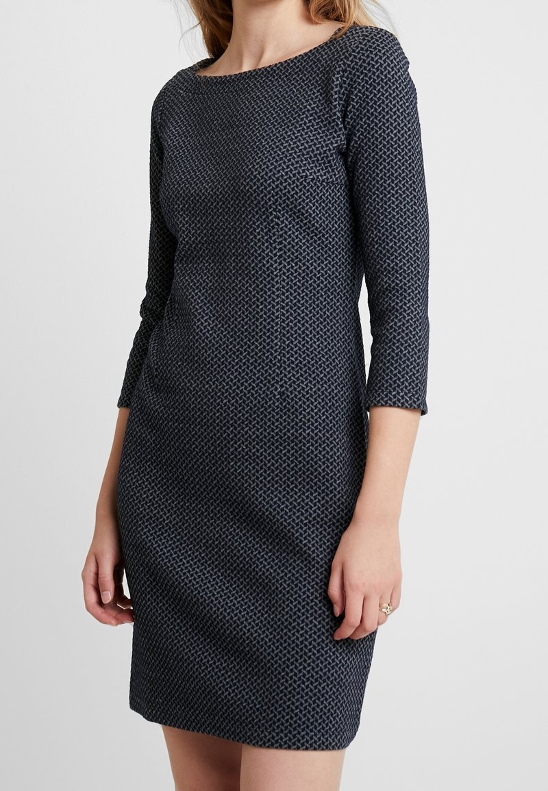Tummansininen mekko, jossa on kolmen neljäsosuuden hihat, teksturoitu geometrinen kuvio, tiukka siluetti, pyöreä pääntie ja keskipituiset hameen pituus.