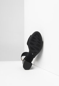 Sandalo nero con tacco, realizzato in pelle liscia e suola in gomma testurizzata, con tacco quadrato e accenti di design minimalista.