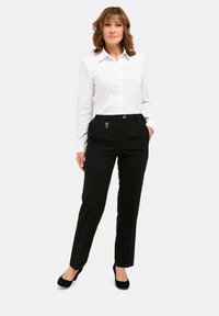 Zwarte op maat gemaakte broeken met zijzakken en zilveren hardwareaccenten, gecombineerd met een goed passend wit overhemden. Glad stoftextuur.