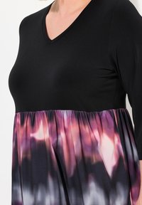 Maglietta nera con scollatura a V e maniche a tre quarti; presenta un orlo in tessuto multicolore arricciato in una gradazione di viola, rosa e nero.