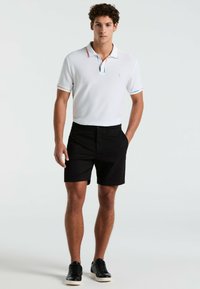 Wit poloshirt met meerkleurige gestreepte accenten, gecombineerd met zwarte shorts en zwarte sneakers. Beschikt over een textuurstof en logo-detail.