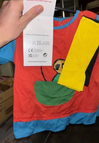 Maglietta per bambini rossa, blu e verde con una tasca. Realizzata con il 80% di poliestere e il 20% di cotone. Presenta un design a cartone animato con occhi rotondi.