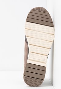 Brun mockaskinnssula med ett texturerat gummimönster. Har spår och kanter för grepp. Ljus beige mellansula kontrasterar med den mörkare yttersulan.