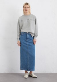 Felpa grigia con la scritta "Marc O'Polo", abbinata a una gonna maxi in denim blu e mocassini chiari. Design dell'outfit semplice e casual.